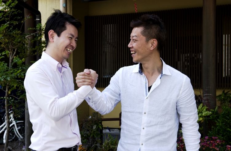 乙村と谷井が笑顔で手を組んでいる